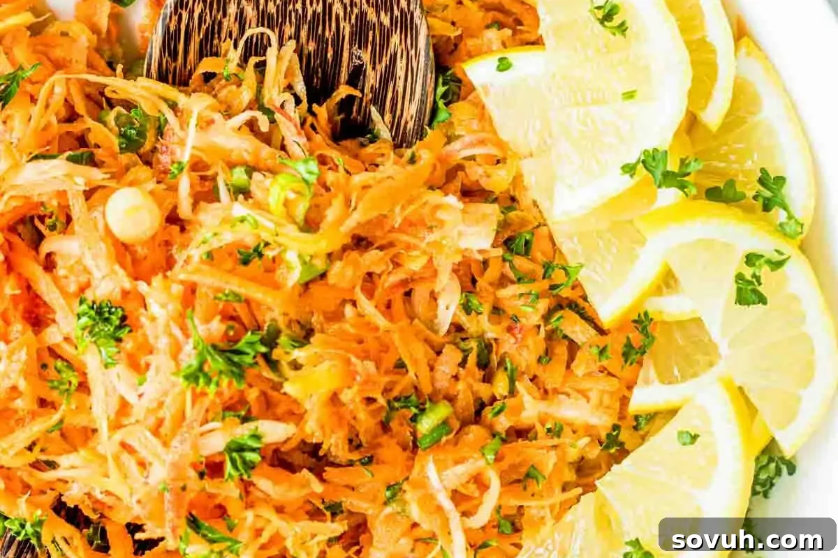 A plate of shredded carrot salad garnished with lemon slices and parsley, served with wooden utensils.