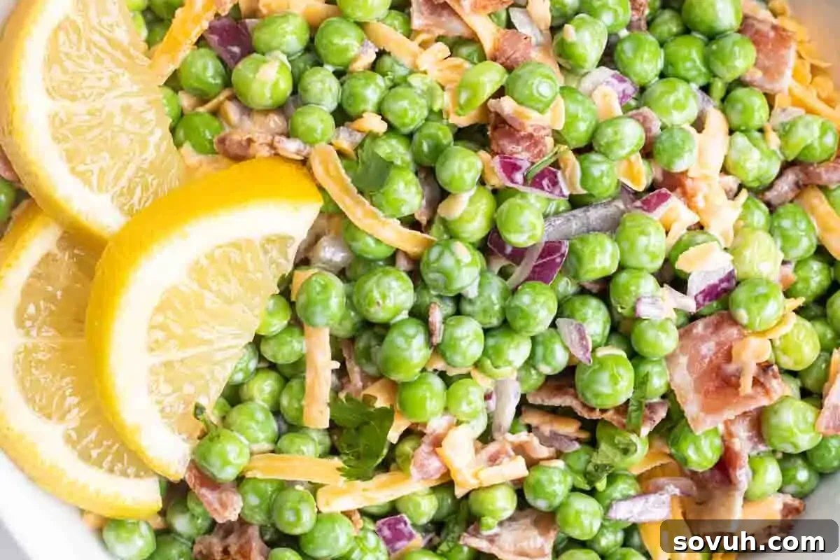 a white bowl of english pea salad garnished with fresh lemon slices