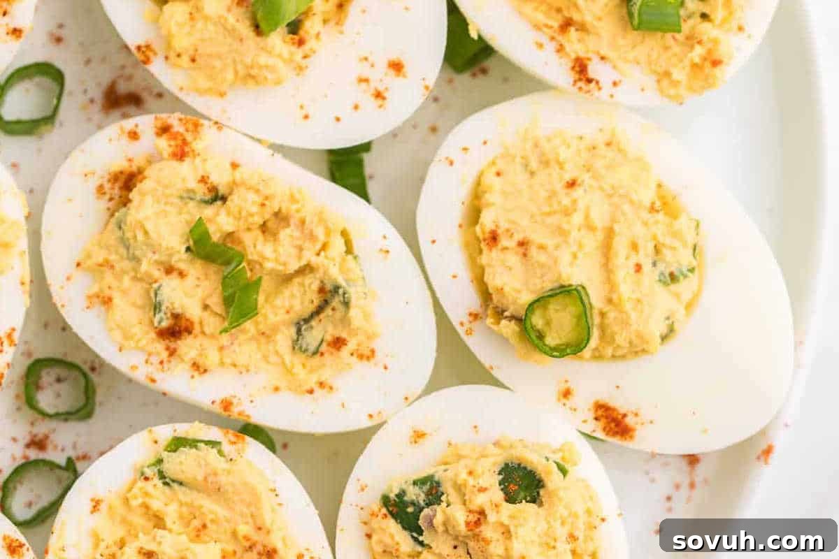Deviled eggs topped with sliced green onions and sprinkled with paprika on a white plate.
