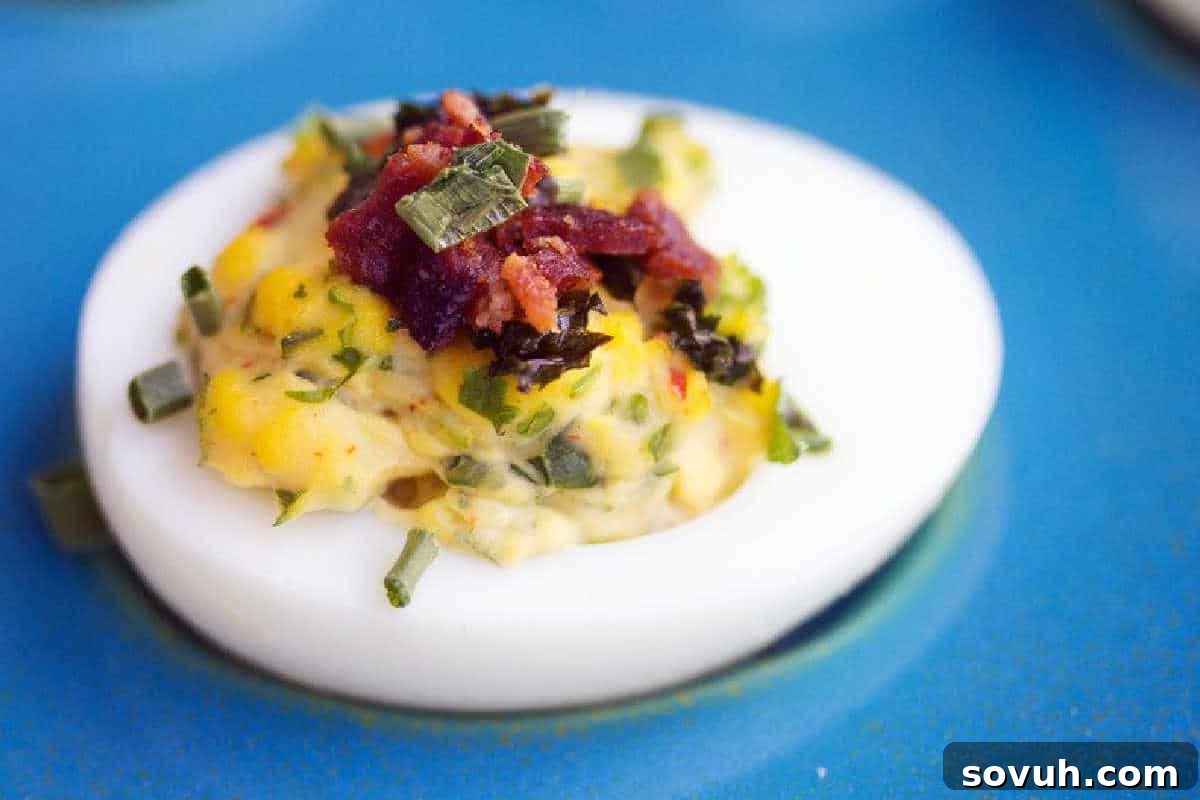 A deviled egg topped with chopped chives and bacon bits on a blue plate.