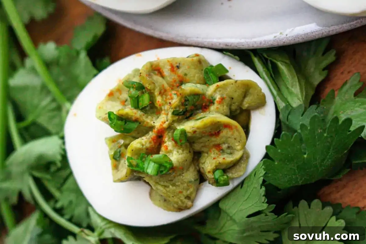 A halved egg with green filling, topped with chopped onions and sprinkled with paprika, surrounded by fresh green herbs.