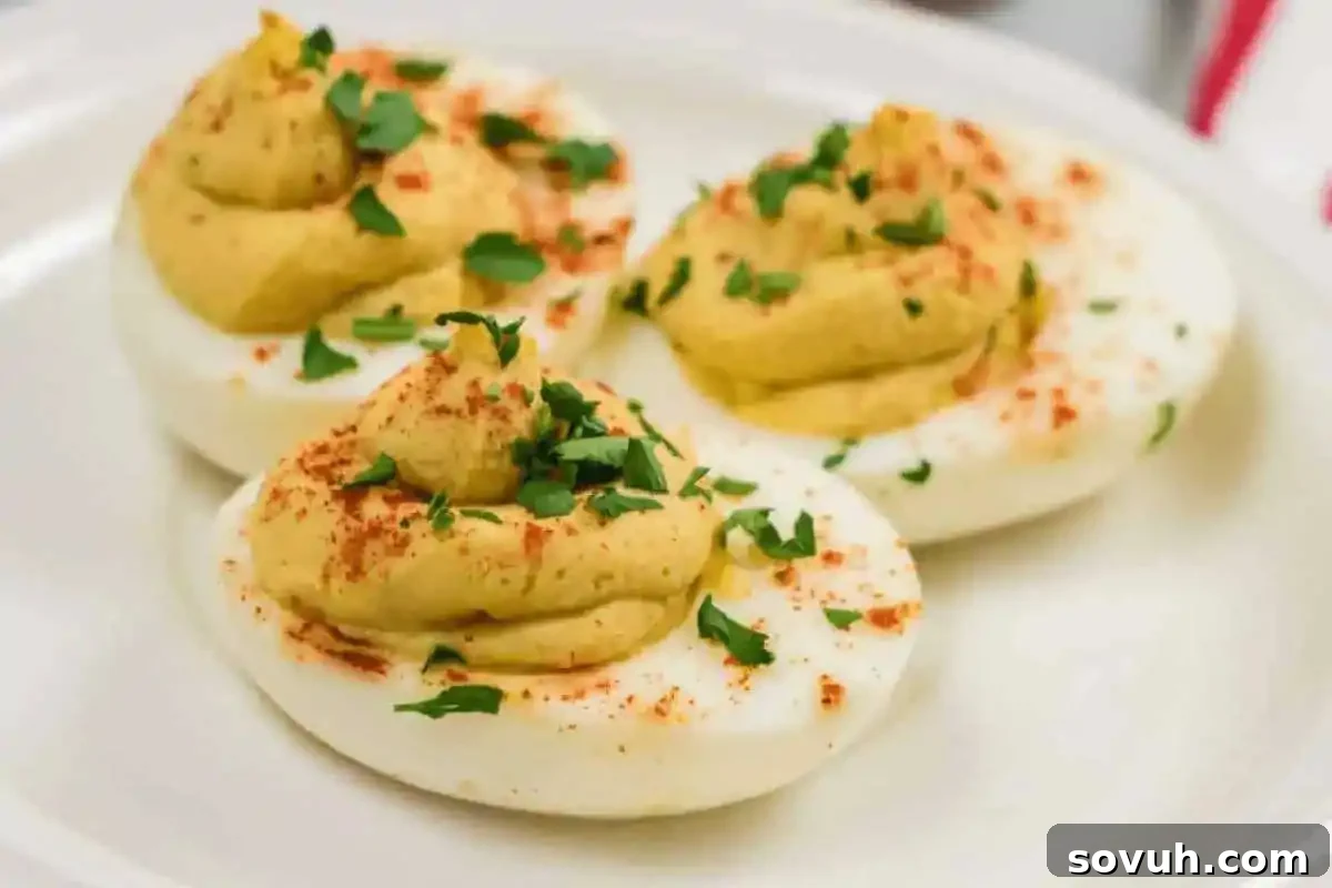 Three deviled egg halves topped with paprika and chopped parsley on a white plate.