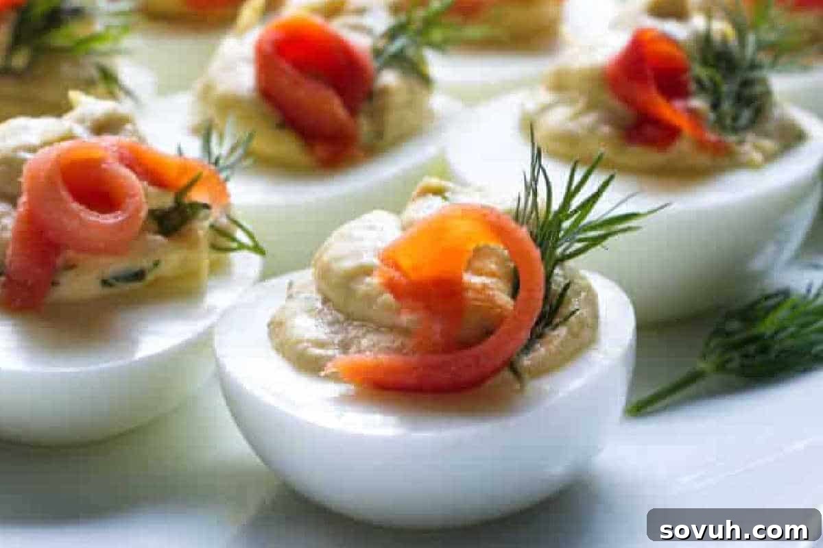 Deviled eggs topped with slices of smoked salmon and dill, arranged on a white surface.