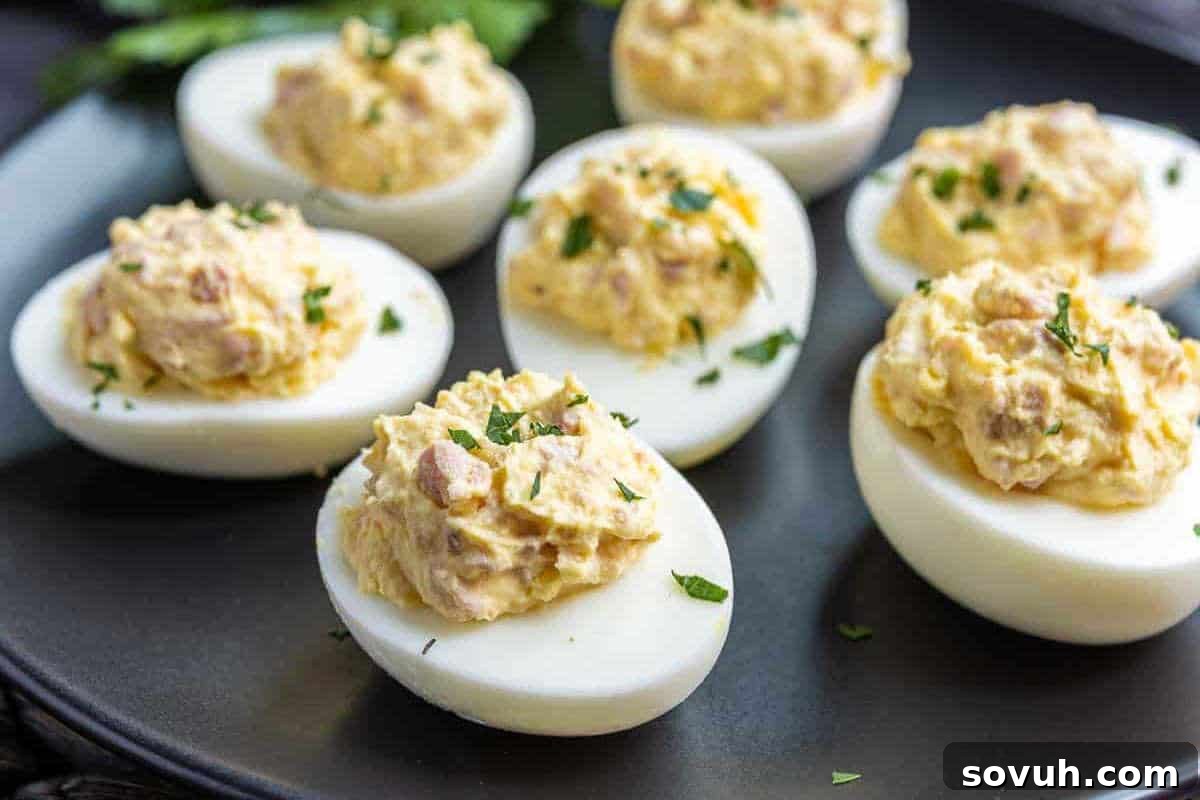 Five halved deviled eggs topped with seasoned filling and garnish are arranged on a dark plate.