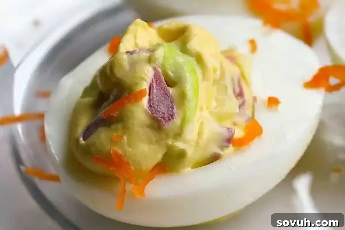 A halved deviled egg filled with a creamy mixture, featuring visible bits of purple onion and orange shredded carrot on top, placed on a white plate.