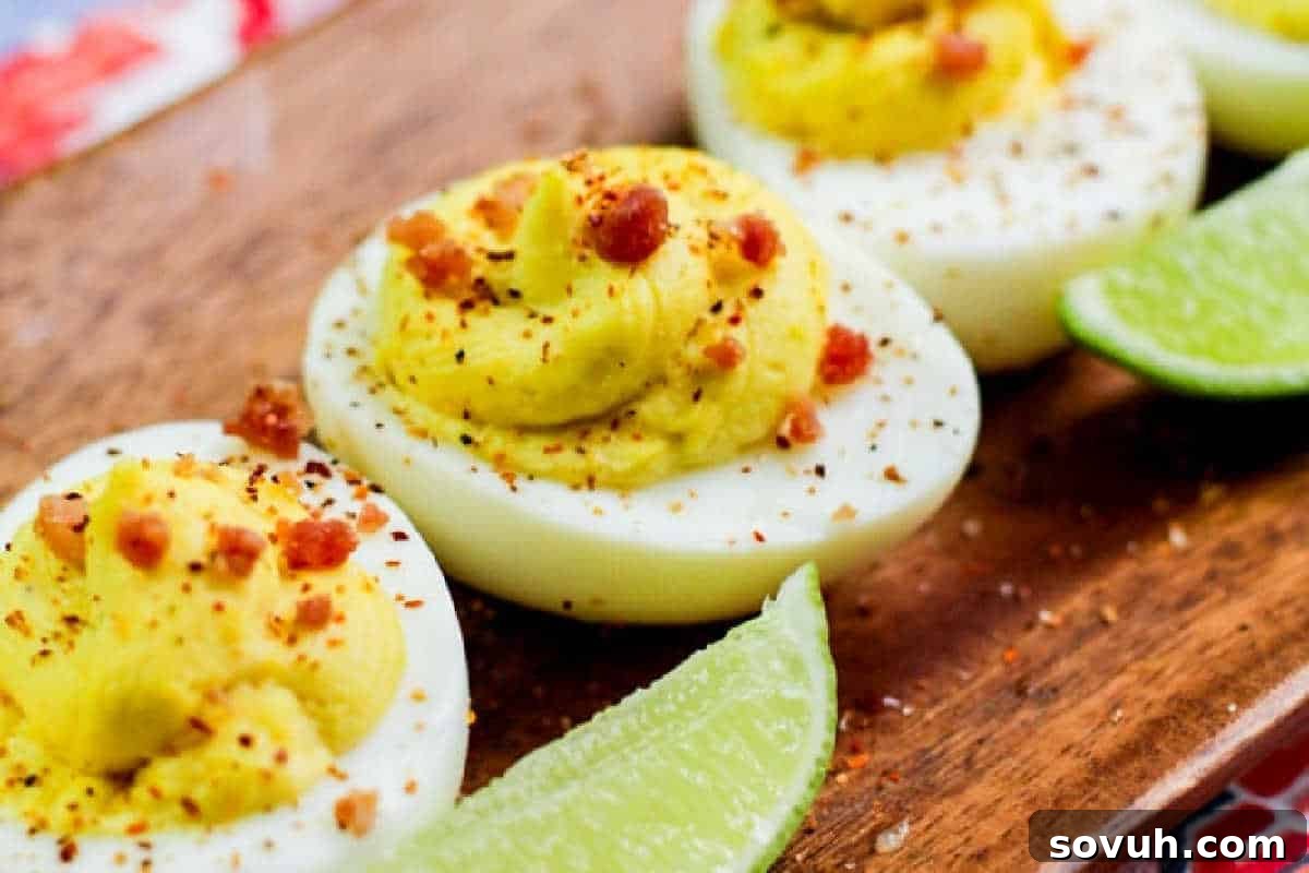 Deviled eggs topped with spices and bacon bits on a wooden board, served with lime wedges.