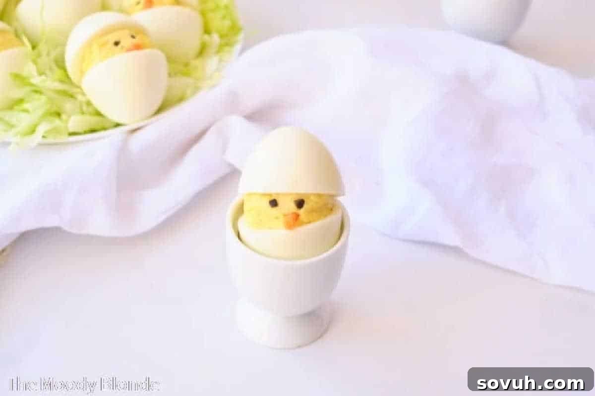 An egg-shaped dish features a chick made from deviled eggs, set in an egg cup, with a towel and more chick eggs in the background.