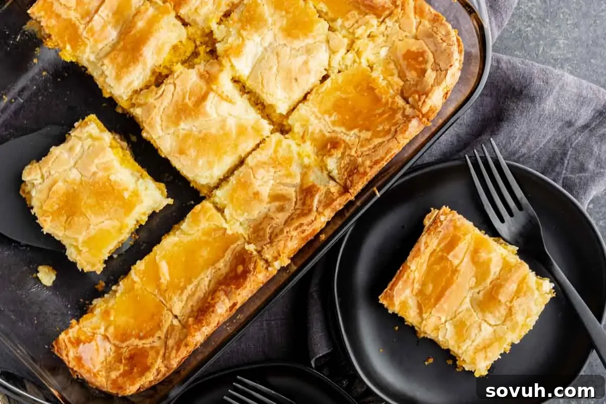 Golden brown dessert bars in a baking dish, with one piece on a black plate alongside a fork on a gray napkin, highlighting their inviting texture and rich color.