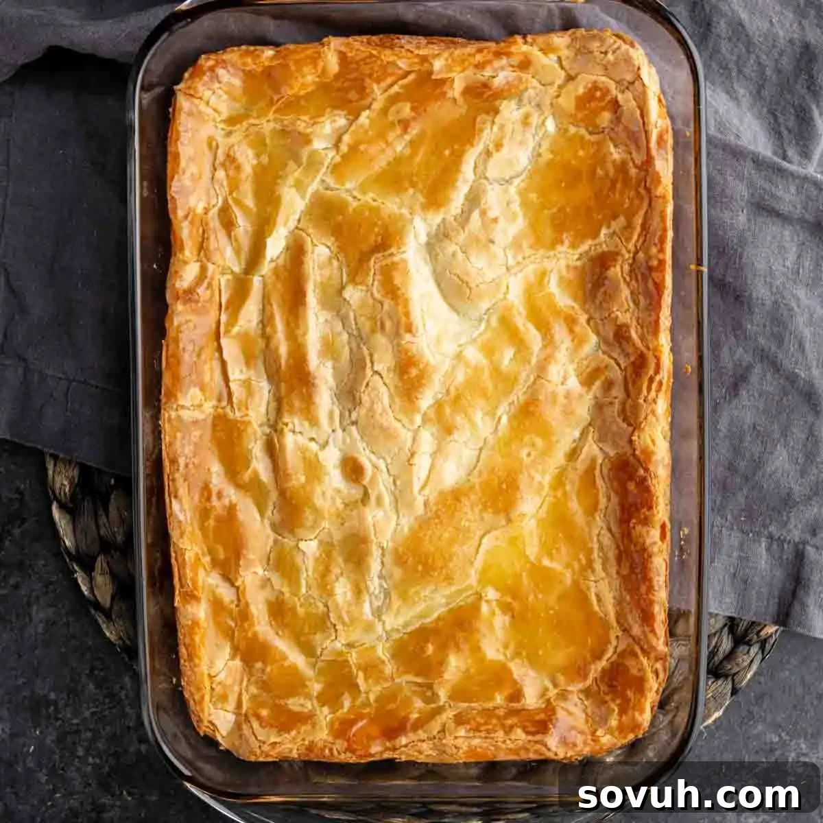 Golden, flaky pie crust in a rectangular glass baking dish on a dark woven surface, ready for baking.