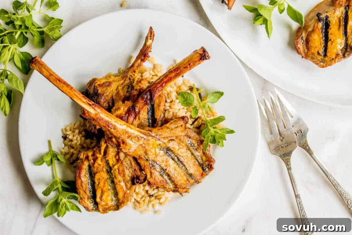 Grilled lamb chops on a bed of rice, garnished with green herbs, on a white plate. Two forks are placed beside the plate.