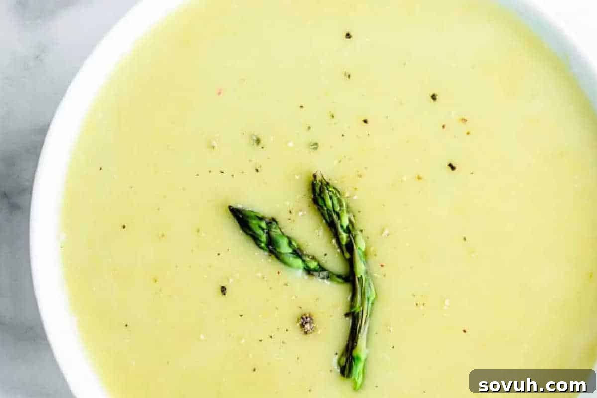 A bowl of creamy asparagus soup garnished with two asparagus spears and sprinkled with black pepper.