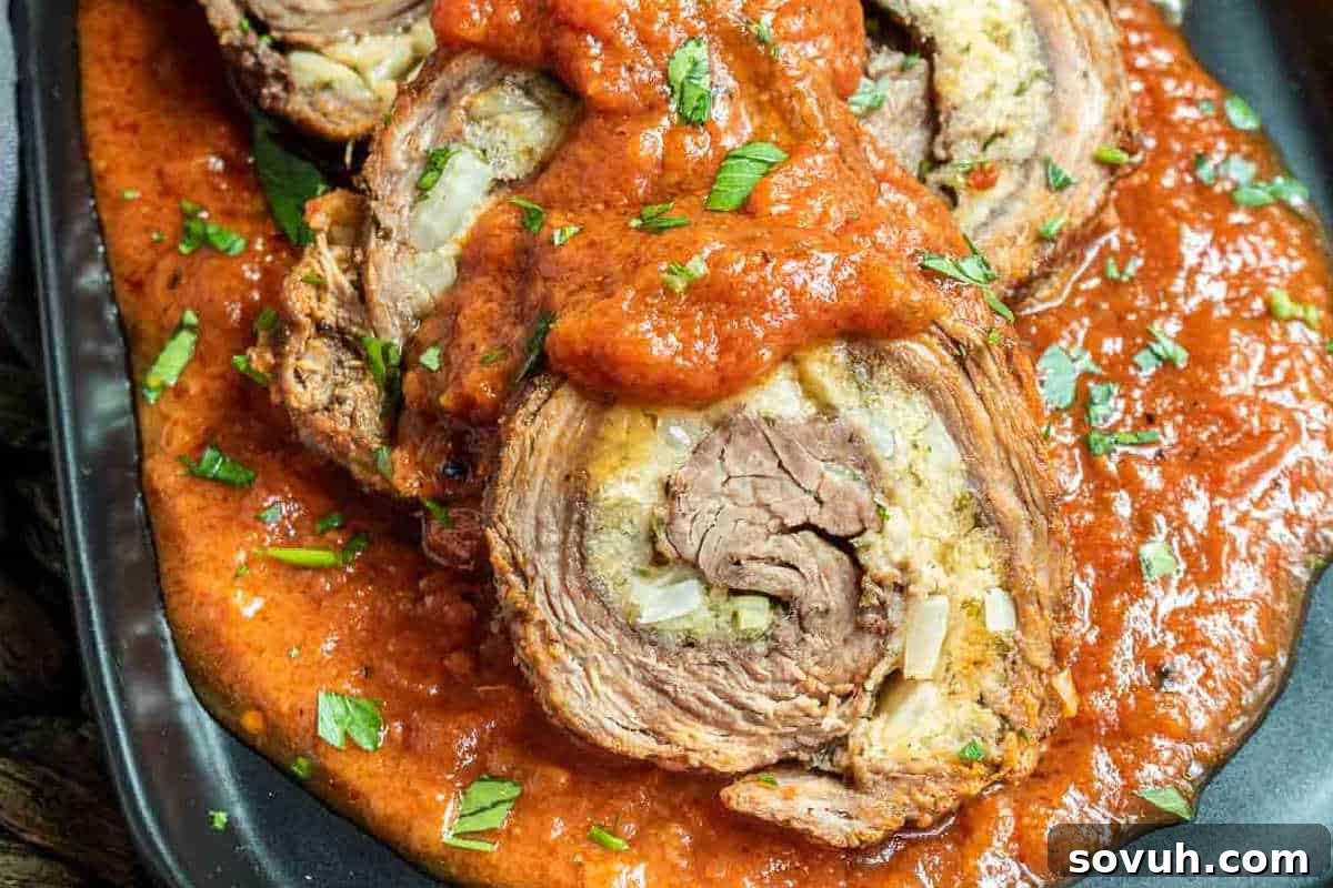 Rolled steak slices topped with tomato sauce and garnished with chopped herbs on a black plate.