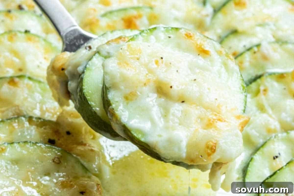A spoon scoops a serving of creamy baked zucchini and cheese, showcasing a golden-brown crust and melted cheese.