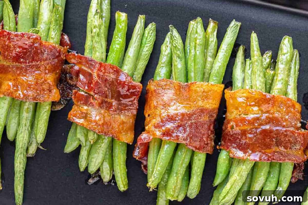 Green beans bundled with crispy bacon strips arranged in a row on a dark surface.