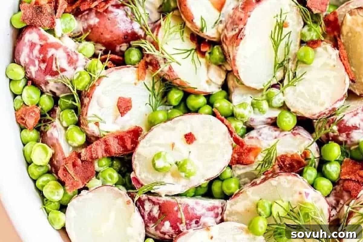 A dish of sliced red potatoes, green peas, and bacon bits garnished with dill.