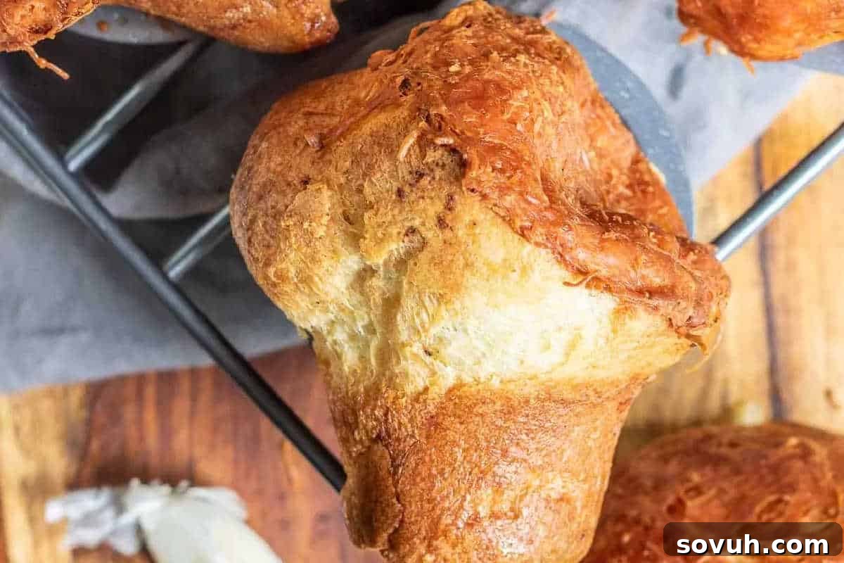 Close-up of a golden-brown popover with a crispy cheese crust, resting on a gray cloth on a wire rack.