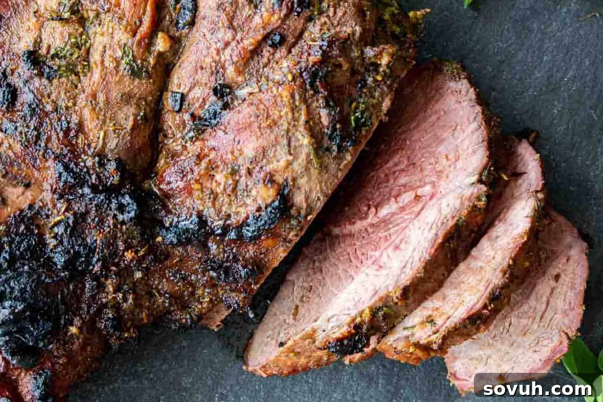 Slices of grilled meat with a charred crust, showing an interior cooked to medium doneness, placed on a dark surface.