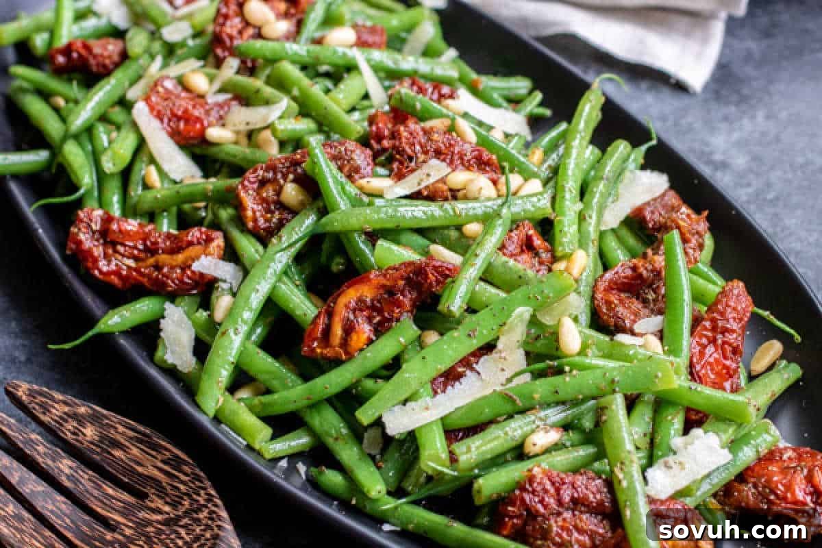 Green bean salad with sun-dried tomatoes, pine nuts, and grated cheese on a black plate.
