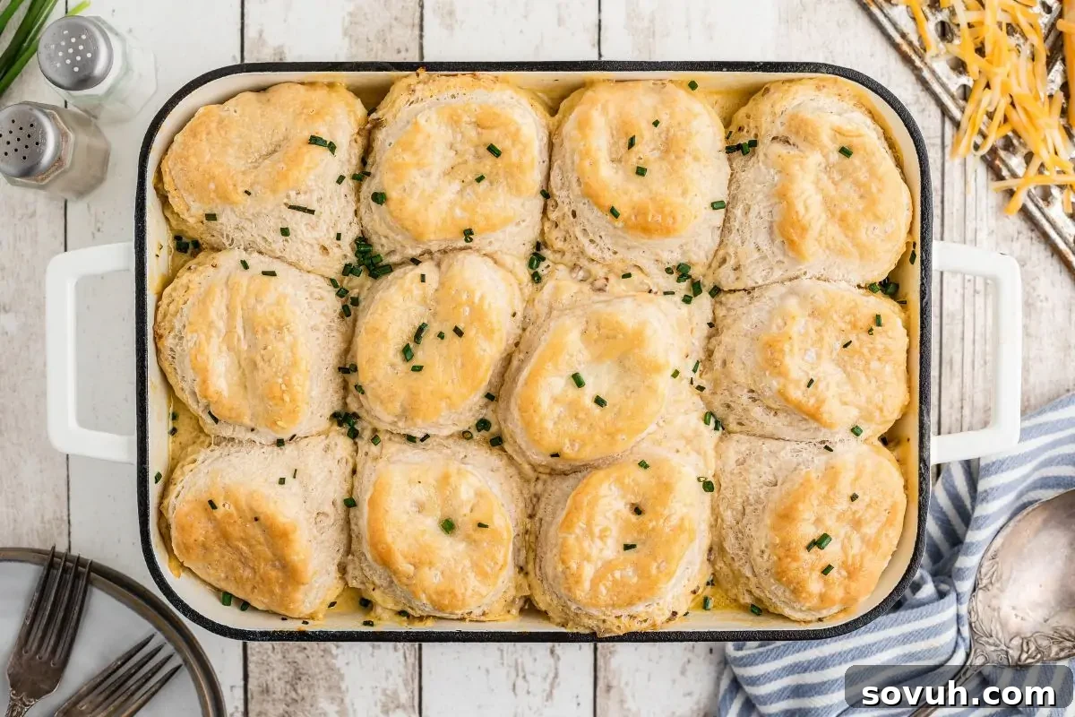 A baking dish containing sausage gravy with golden-brown biscuits, garnished with chopped herbs.