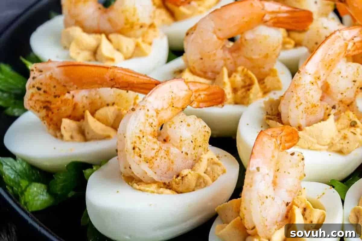 Halved boiled eggs filled with yolk mixture, topped with cooked shrimp and sprinkled with seasoning, on a bed of greens.