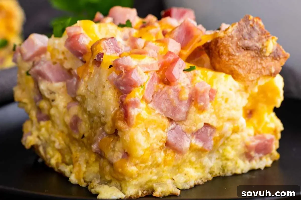A slice of ham egg and cheese bake topped with diced ham and melted cheese, perfect for celebrating Mother's Day, served with a piece of toast.