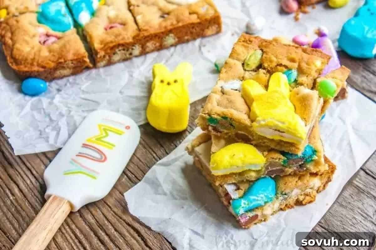 Whimsical Easter Treats Made Simple 2 Colorful dessert bars with candy and marshmallow bunny shapes on parchment, beside a spatula labeled "YUM," on a wooden surface.