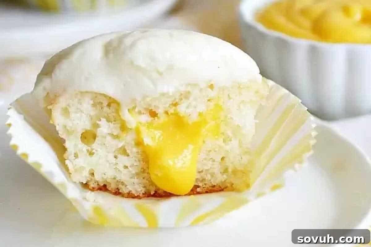 Whimsical Easter Treats Made Simple 11 A cupcake with white frosting is cut open, revealing a yellow filling, on a white wrapper and plate.