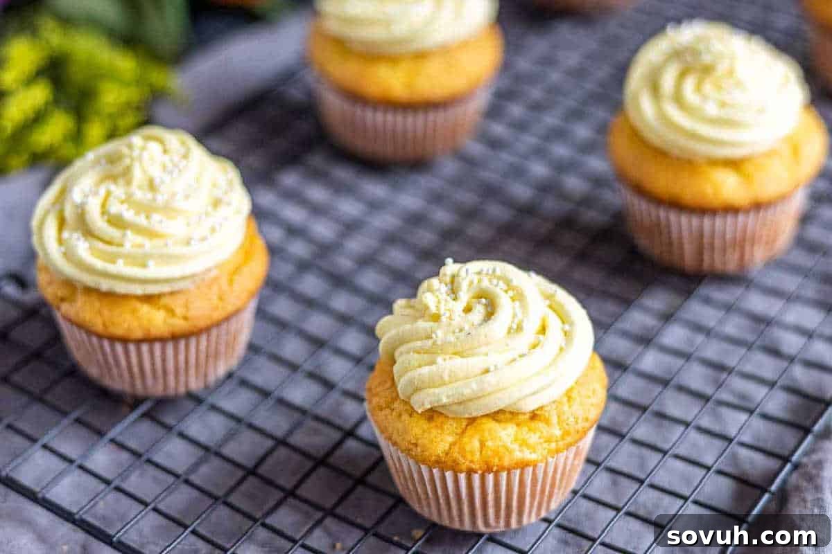Whimsical Easter Treats Made Simple 19 Cupcakes with light yellow frosting are placed on a black wire cooling rack.