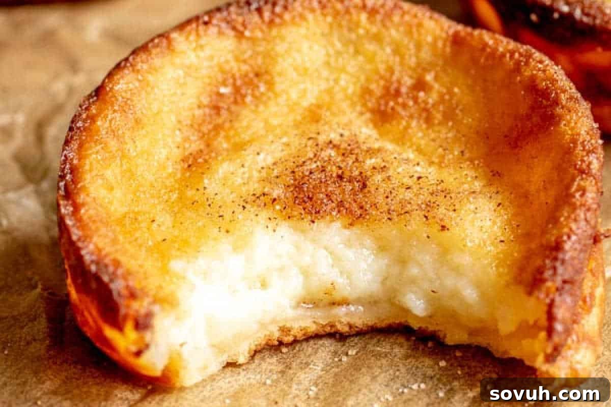 Whimsical Easter Treats Made Simple 20 A partially eaten pastry with a golden, crispy outer layer, revealing a creamy filling, sprinkled with cinnamon on top. Placed on brown parchment paper.