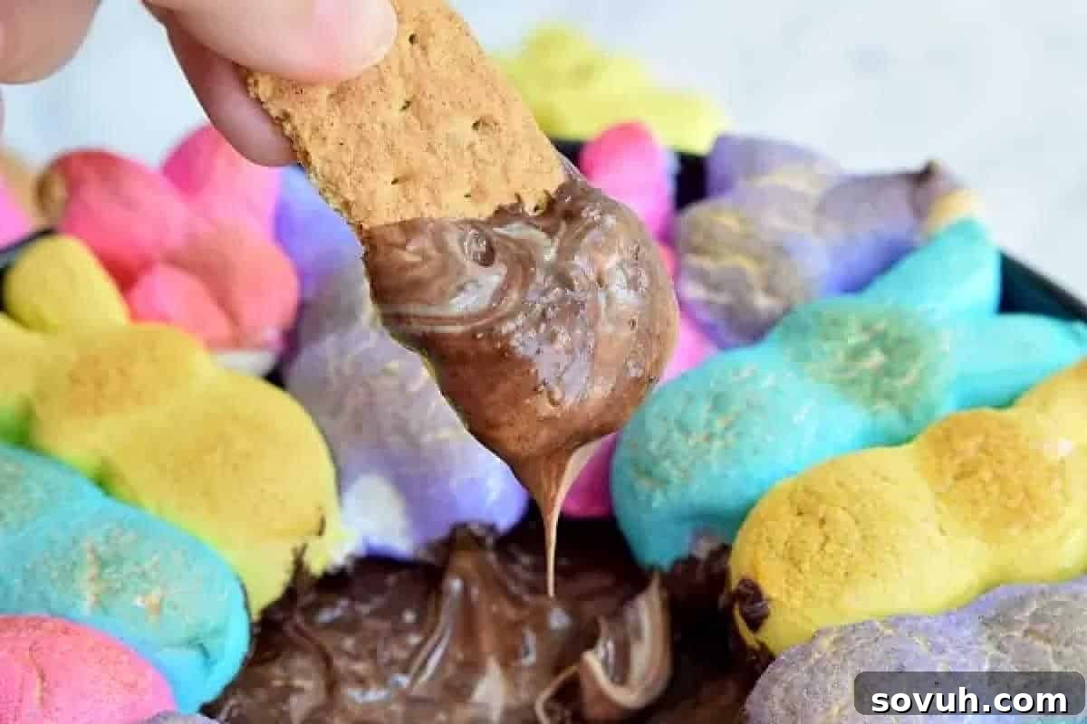 Whimsical Easter Treats Made Simple 5 A cracker being dipped into melted chocolate surrounded by colorful marshmallow shapes in a dish.
