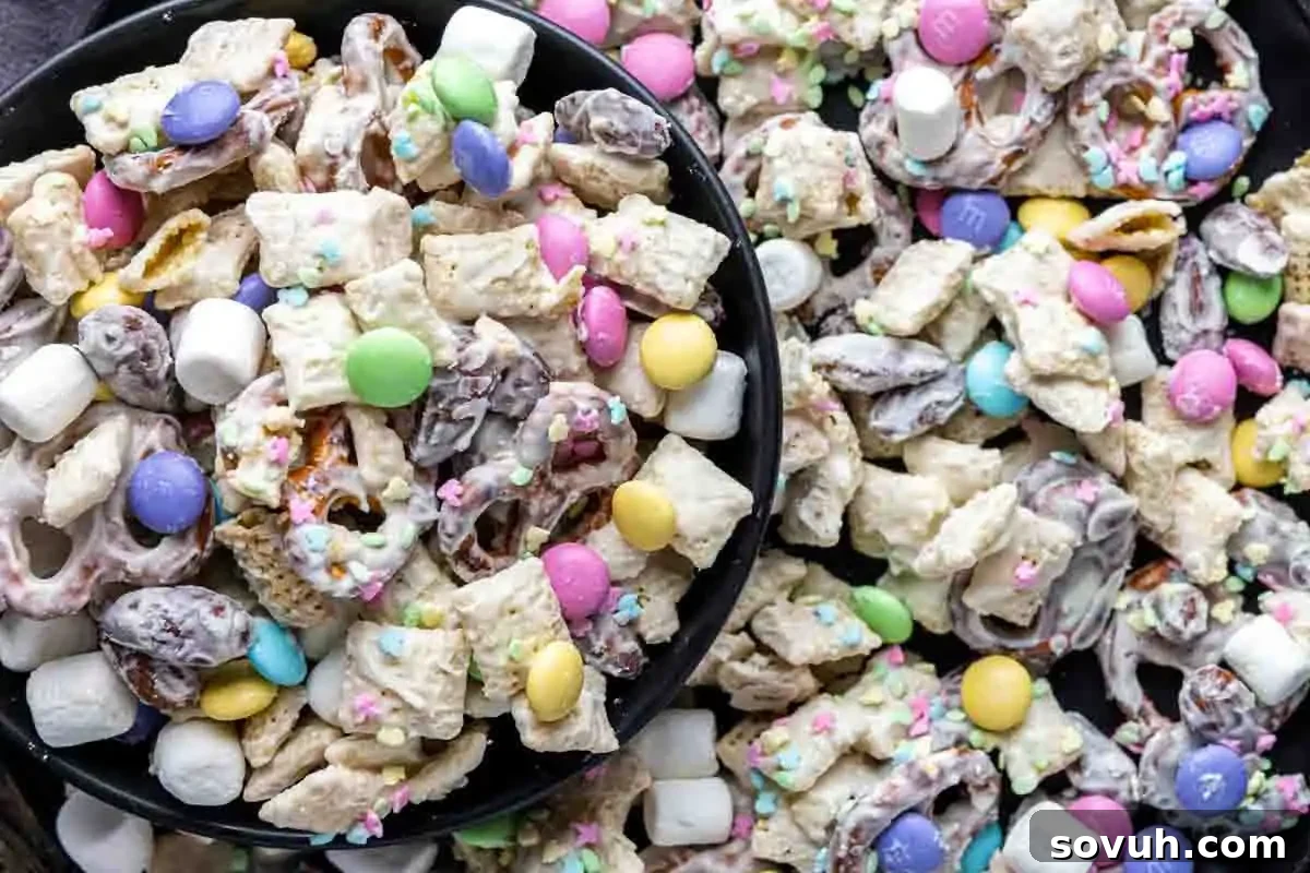 Whimsical Easter Treats Made Simple 6 Close-up of a snack mix containing pretzels, cereal squares, chocolate candies, mini marshmallows, and sprinkles, coated in a white glaze.