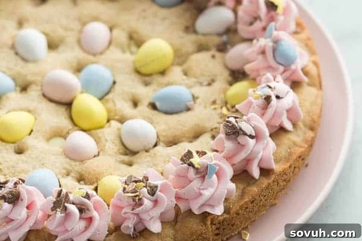 A large cookie topped with pastel-colored chocolate eggs and decorated with pink frosting along the edge.