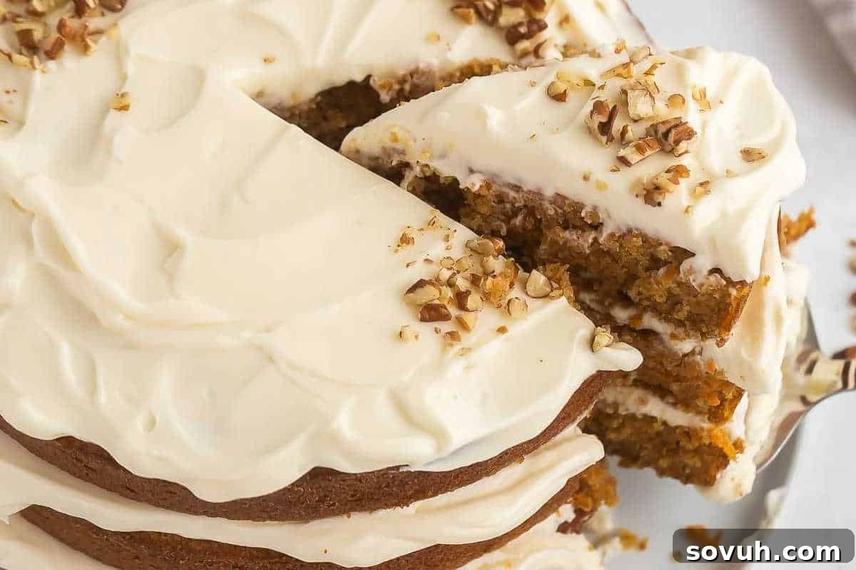 A layered cake with cream cheese frosting and chopped nuts on top. A slice is being lifted from the cake.