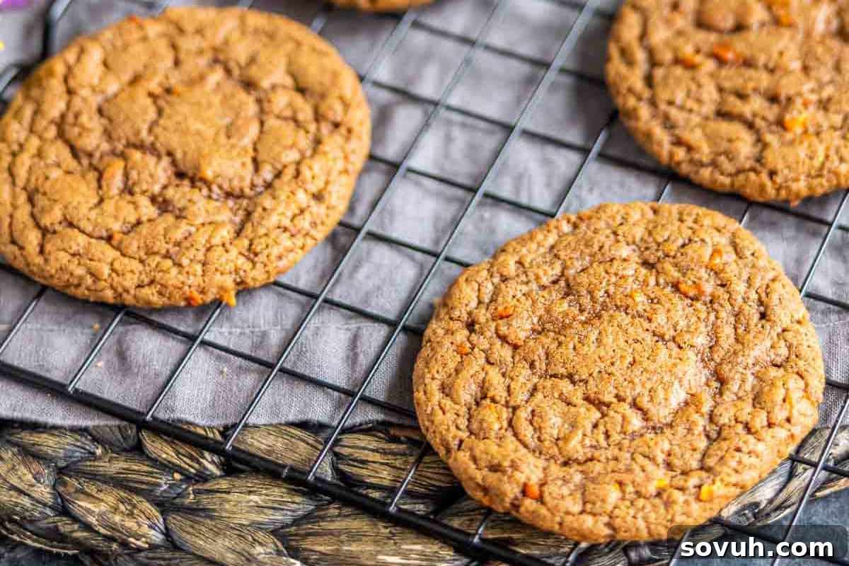 A close-up photograph showcasing several freshly baked Carrot Cake Mix Cookies, perfectly arranged on a wire rack to cool. The cookies exhibit a slightly crisp texture around their golden-brown edges, hinting at their delicious flavor and indicating they are ready to be enjoyed.