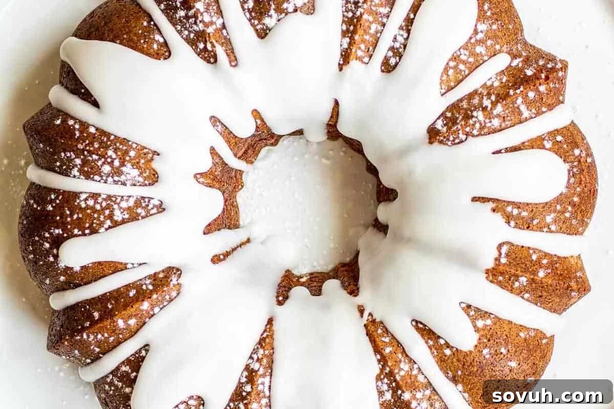 A beautifully baked round bundt cake, generously drizzled with glistening white icing and delicately dusted with a light layer of powdered sugar, showcasing its intricate design and inviting texture.