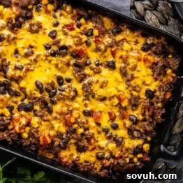 A casserole dish filled with a baked mixture of ground beef, black beans, corn, tomatoes, and melted cheddar cheese.