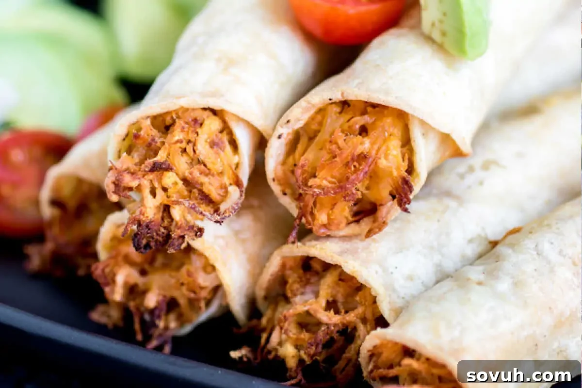 A close-up of crispy Baked Chicken Taquitos, beautifully arranged on a white plate, elegantly garnished with refreshing sliced cucumbers and bright cherry tomatoes. This vibrant presentation highlights the golden texture of the taquitos and their fresh accompaniments, making for an inviting meal.