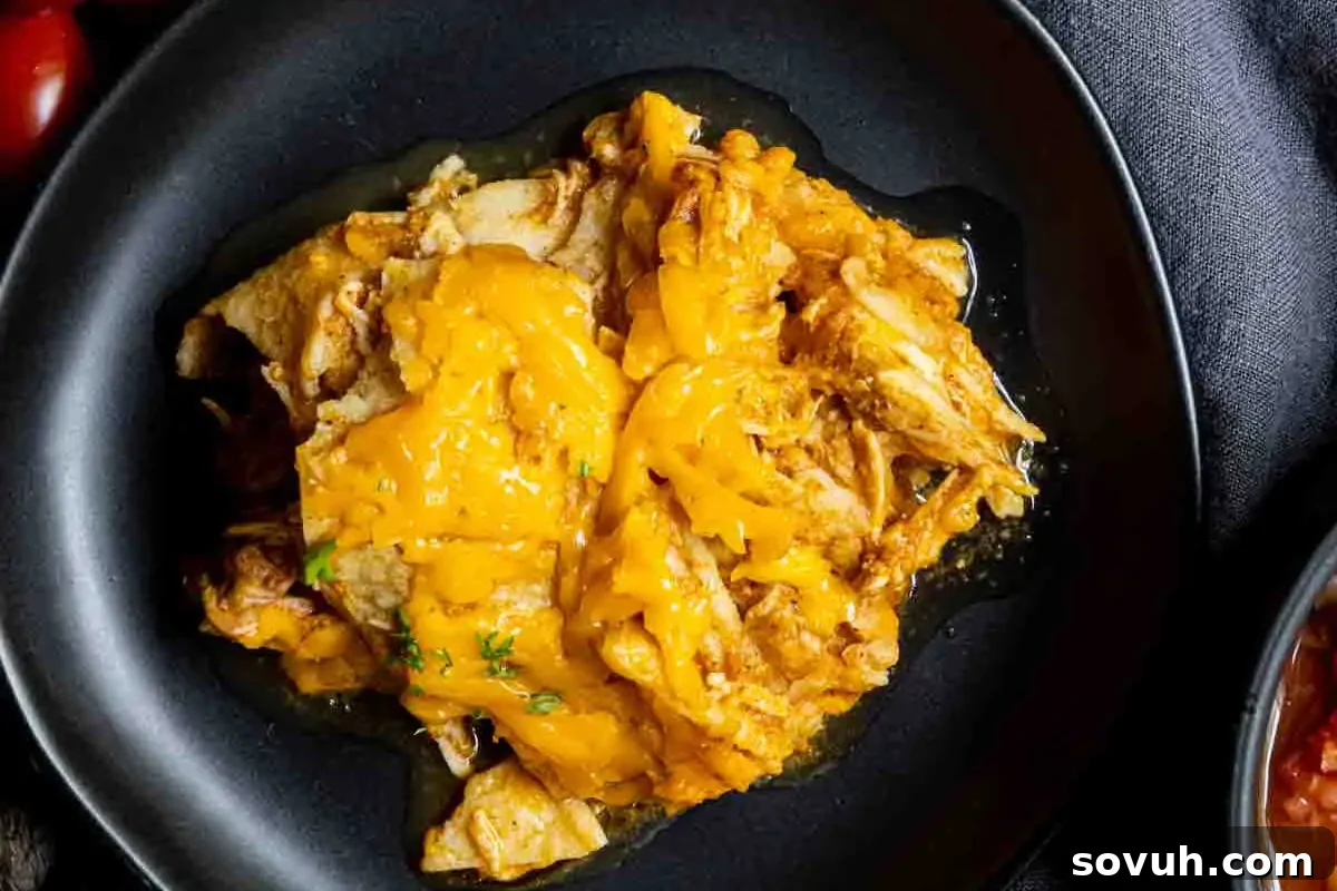 A rustic black skillet filled with deliciously shredded chicken, generously topped with a blanket of melted cheddar cheese and garnished with fresh herbs, all set against a dark textured background. This image captures the comforting and rich appeal of slow-cooked chicken enchiladas.