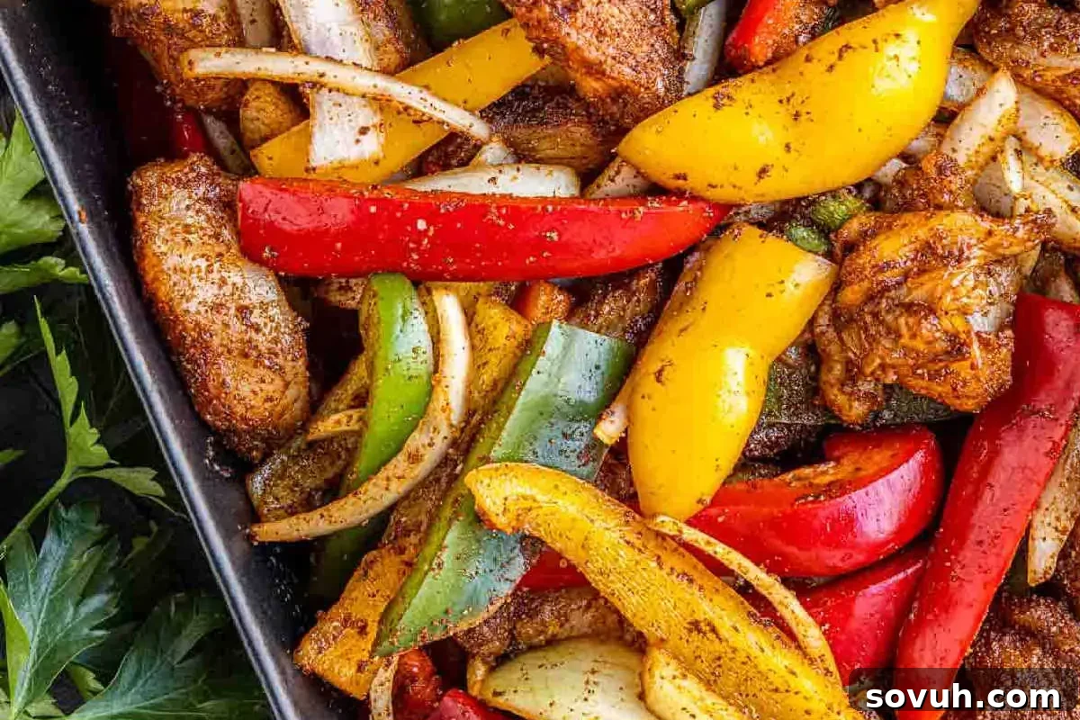 A close-up shot of a rustic black dish filled with perfectly seasoned chicken strips, brilliantly colored sliced red, yellow, and green bell peppers, and tender onion wedges. This vibrant and aromatic ensemble showcases a delicious and healthy meal ready to be enjoyed.