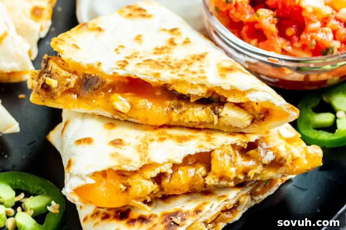 A tantalizing close-up of a golden-brown chicken quesadilla, bursting with melted cheese and succulent chicken, elegantly presented on a black plate alongside a vibrant dollop of salsa and garnished with fresh, thinly sliced jalapeños. This image captures the crispy texture and delicious filling perfectly.