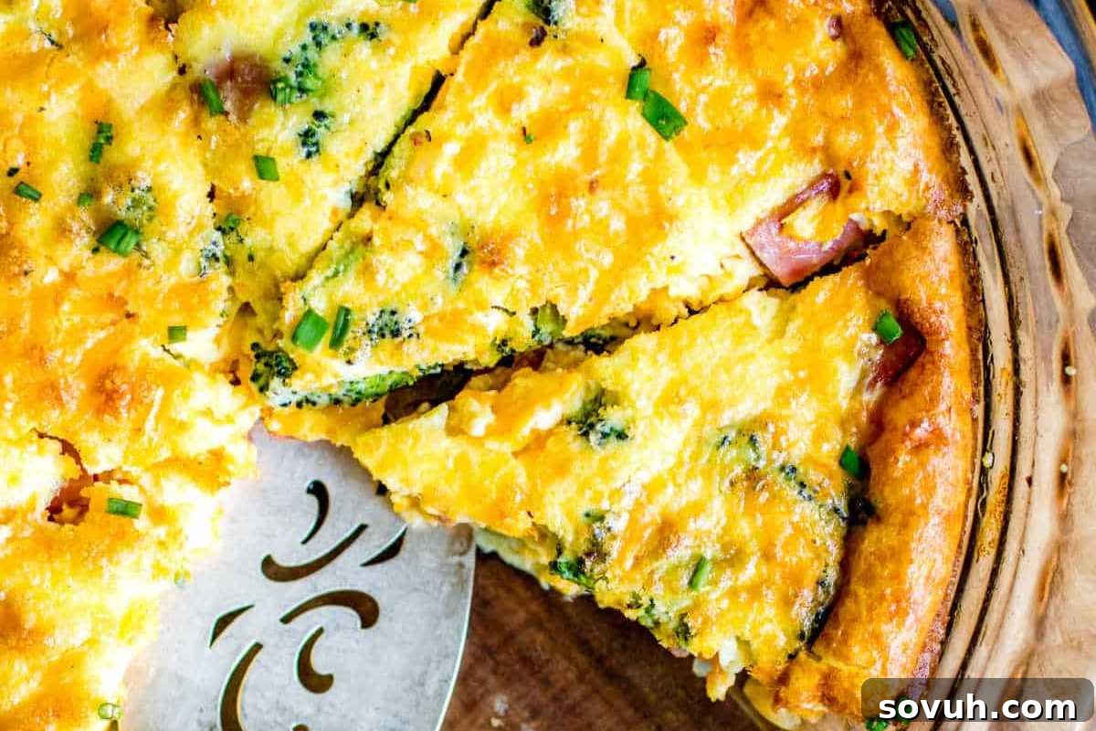 A freshly baked quiche with vibrant chunks of ham and green herbs, sliced and served on a glass pie dish.