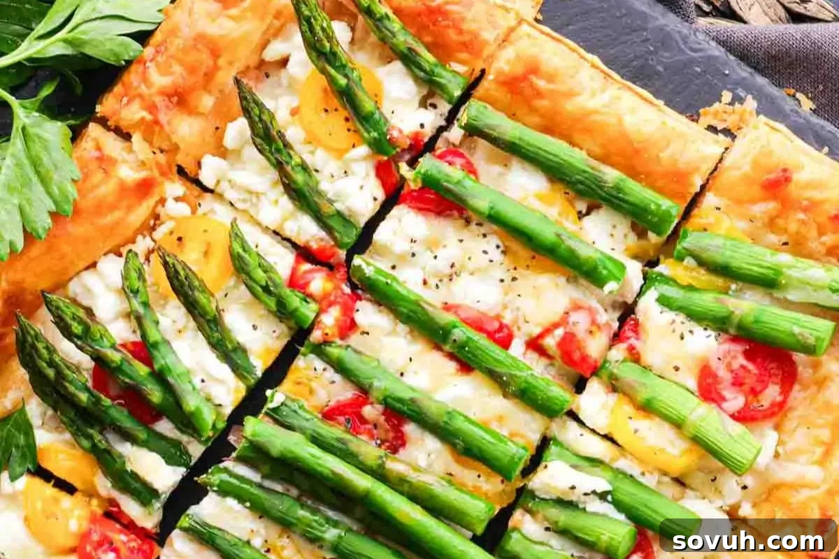 Sliced asparagus and cherry tomato tart , served on a dark slate surface.