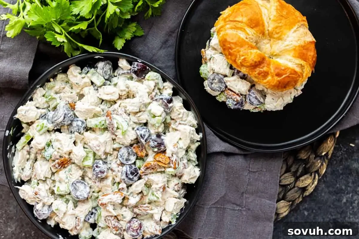 Sweet and Savory Chicken Grape Salad 2 A bowl of chicken salad with grapes and pecans next to a croissant sandwich filled with the same salad, displayed on black plates with parsley garnish nearby.