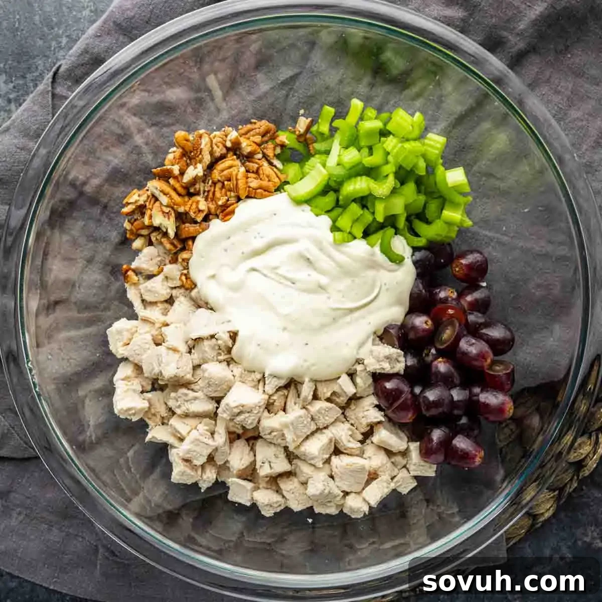 Sweet and Savory Chicken Grape Salad 4 A glass bowl containing diced chicken, chopped celery, halved grapes, pecans, and a portion of creamy dressing, all arranged separately before mixing.
