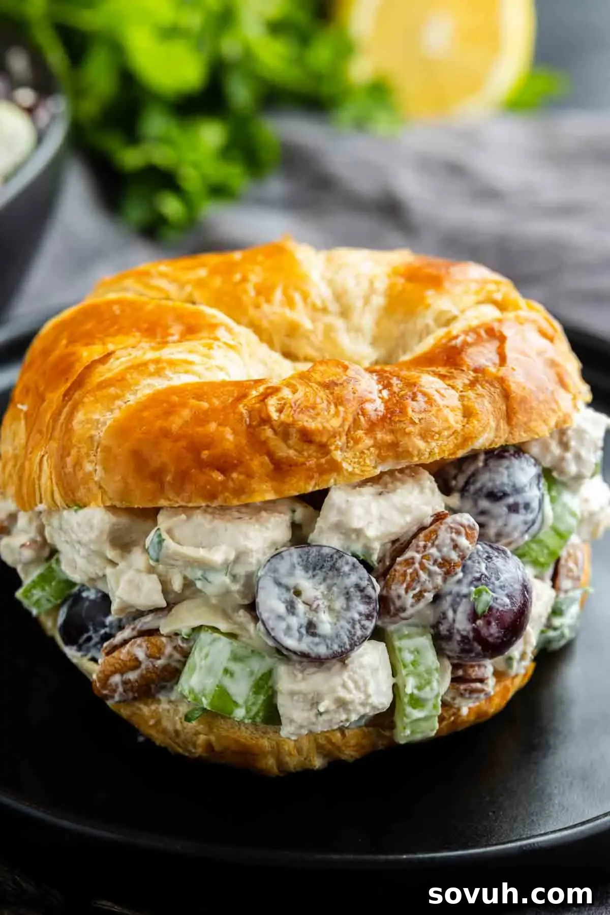Sweet and Savory Chicken Grape Salad 5 A croissant sandwich filled with chicken salad, grapes, celery, and pecans sits on a black plate.