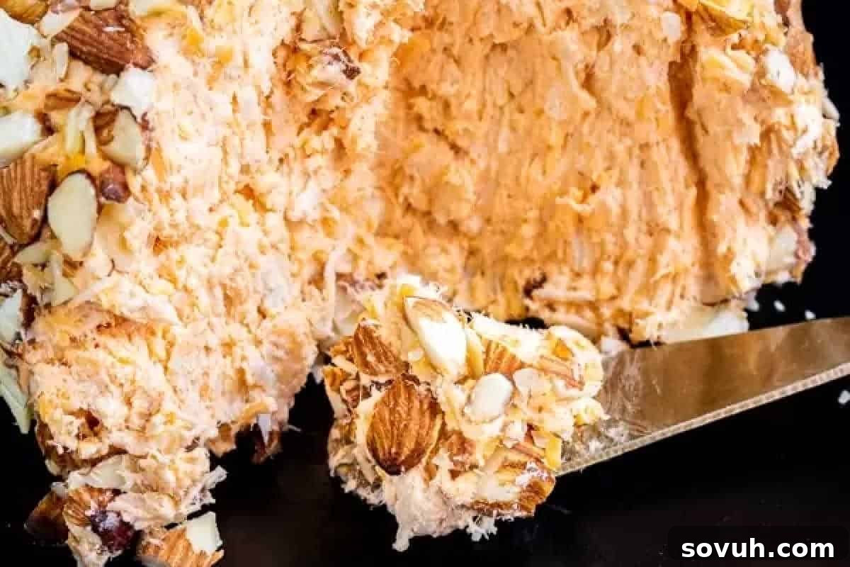 A perfectly portioned slice of a savory cheese ball, beautifully coated with finely chopped nuts, resting on a knife against a subtly dark background, highlighting its rich texture and festive presentation.