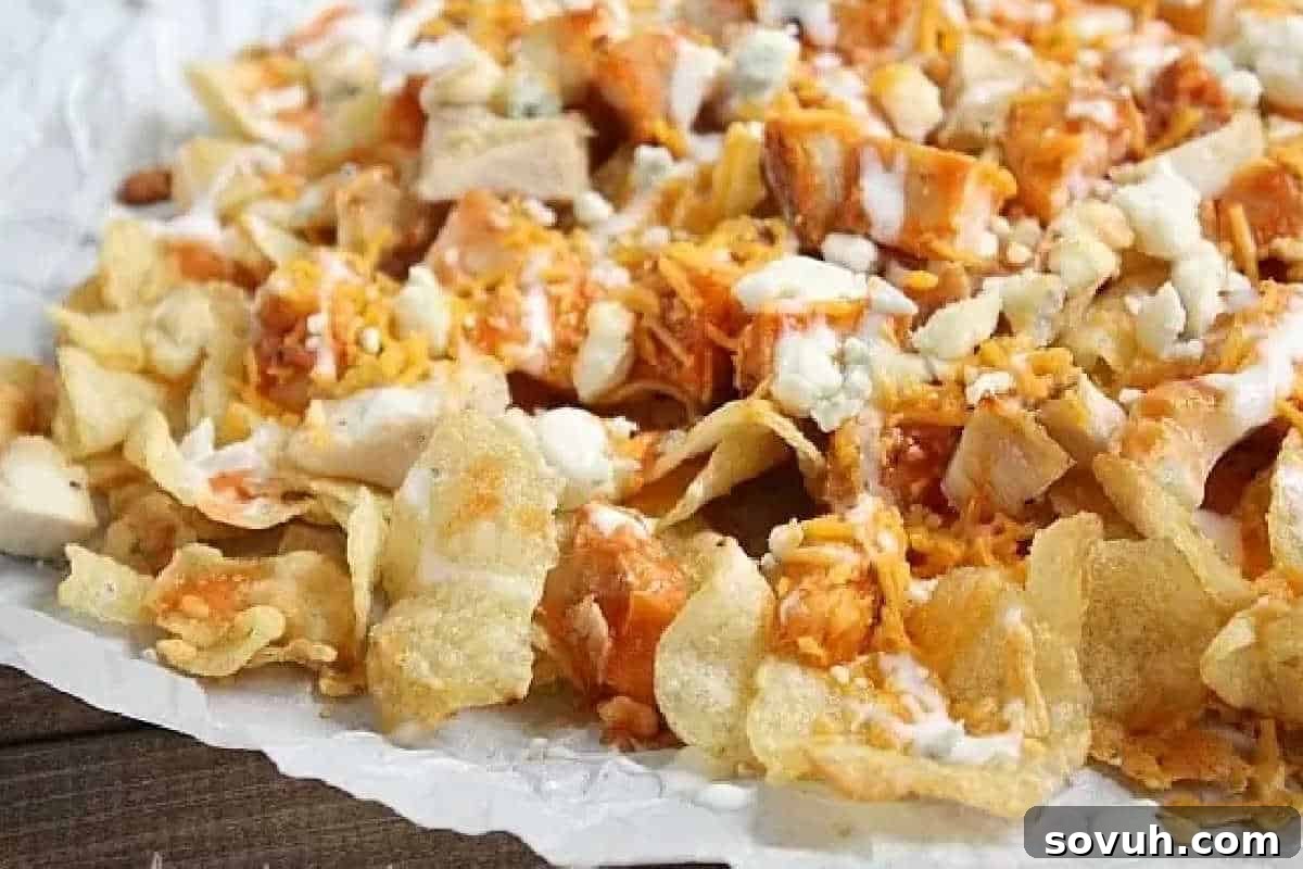 A glorious pile of crispy potato chips (or tortilla chips), generously topped with seasoned diced buffalo chicken, a mix of shredded cheddar and crumbled blue cheese, and a tantalizing drizzle of buffalo sauce, all served on parchment paper.