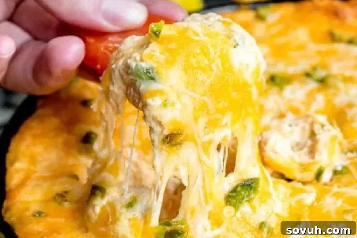 A hand lifts a portion of irresistible, cheesy baked dip, revealing melted cheese and vibrant green peppers, perfectly browned on top and ready to be enjoyed.