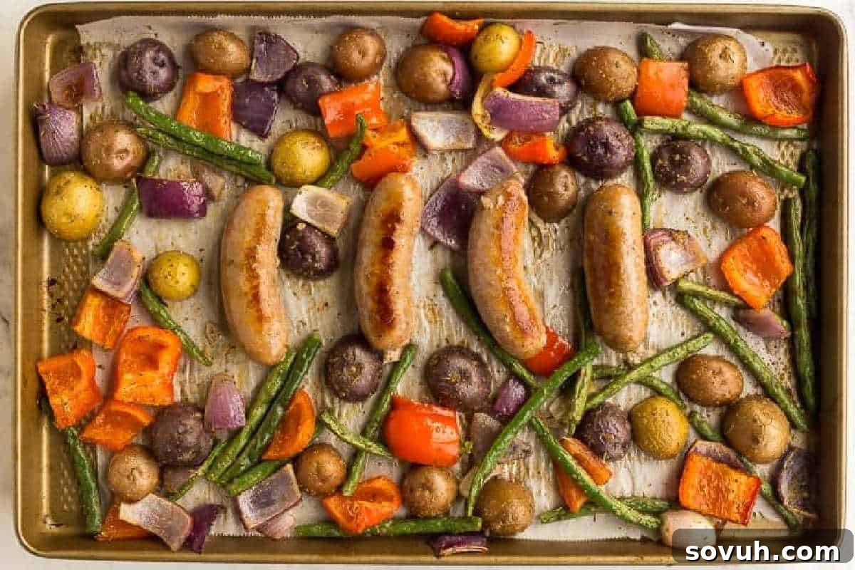 A sheet pan with roasted sausages, baby potatoes, green beans, red bell peppers, and red onions arranged evenly.