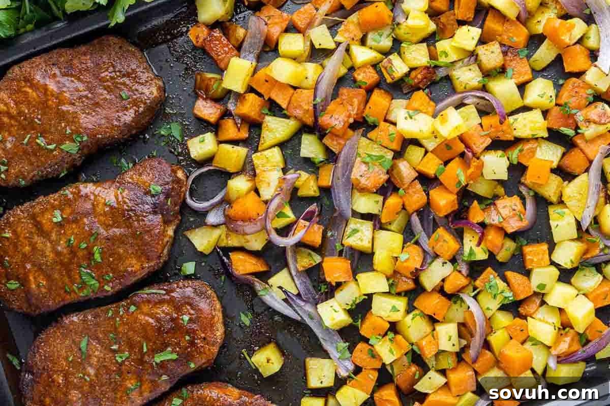 Sheet pan with four seasoned pork chops and a mix of roasted diced sweet potatoes, yellow potatoes, and red onion, garnished with chopped herbs.
